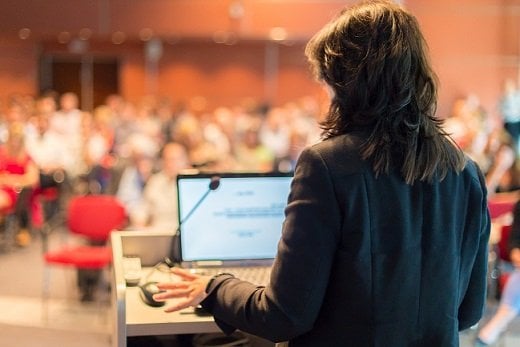 Mujer dando discurso a los asistentes de un evento empresarial organizado